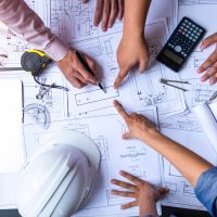 engineers pointing to building on blueprint and using laptop to drawing design building Project in office, construction concept. Engineer concept